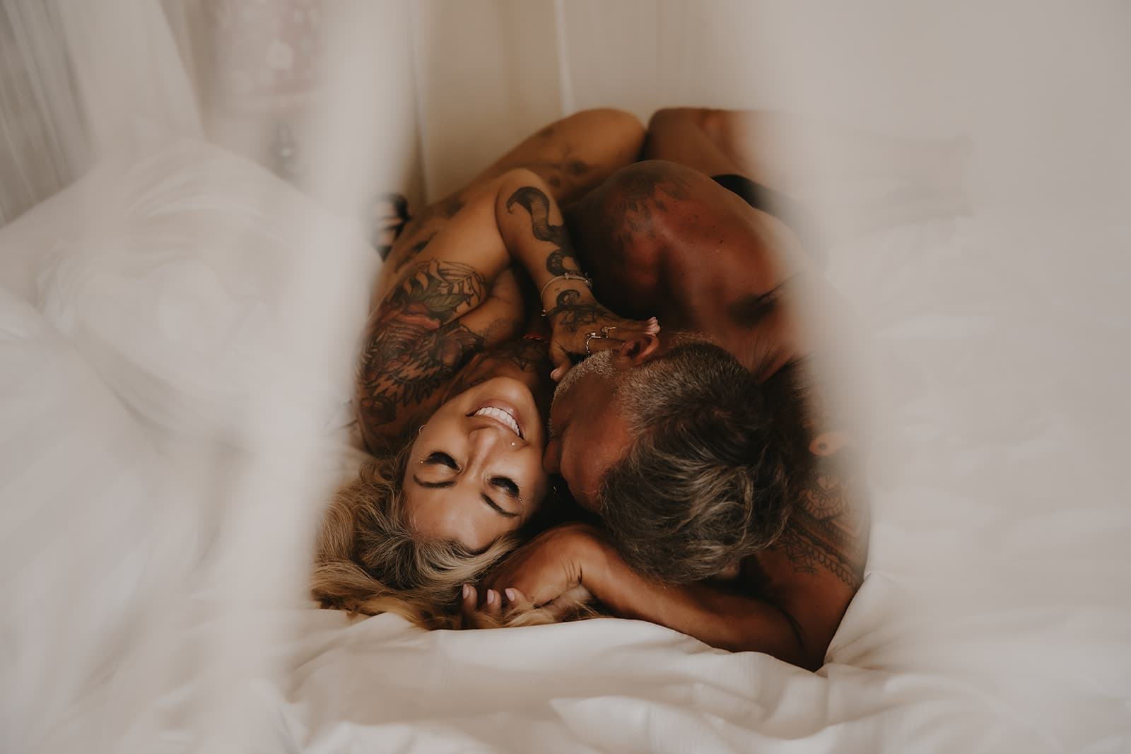 Rex and Rebelle laughing and wrapped around each other in white sheets