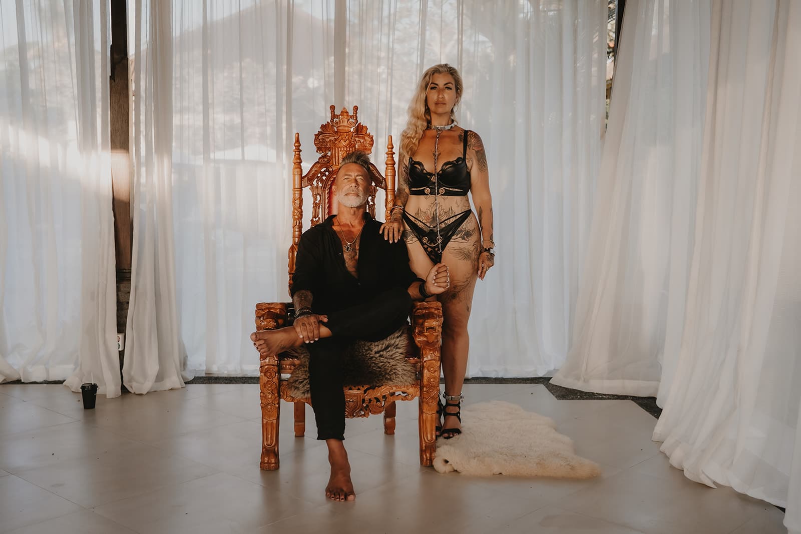 Rex seated on his carved throne with Rebelle standing beside him, her hand on his shoulder, both looking straight at the camera